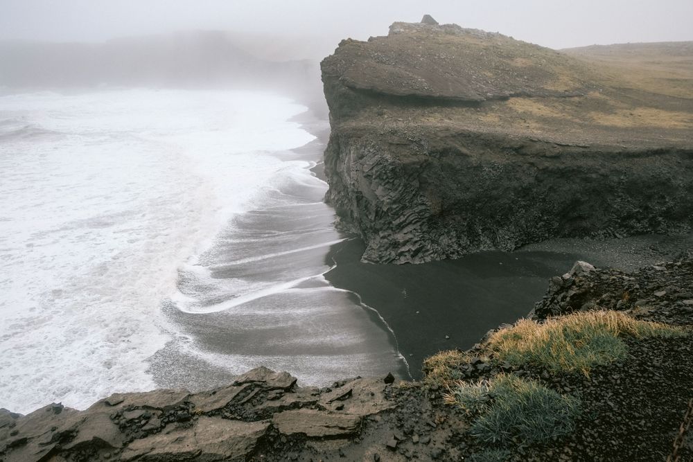 Misty coastline view with dramatic cliffs and rocky beach stretching into the distance.