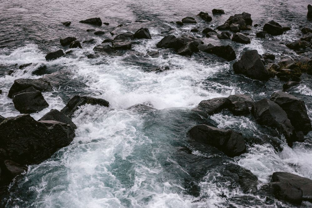 Turbulent ocean waves crash against dark rocky coastline creating white foam patterns.