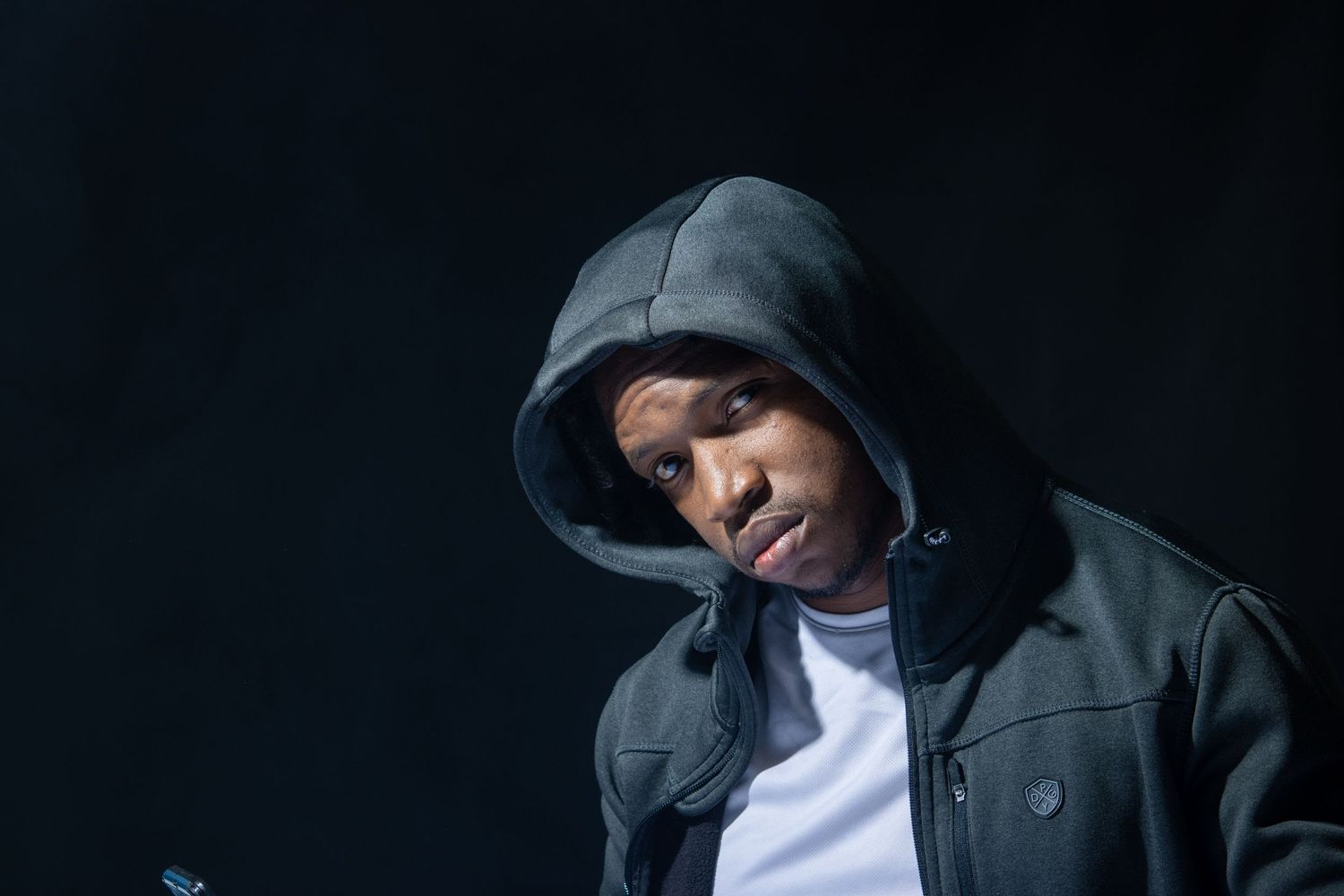 Moody portrait of person wearing black hoodie against dark background.