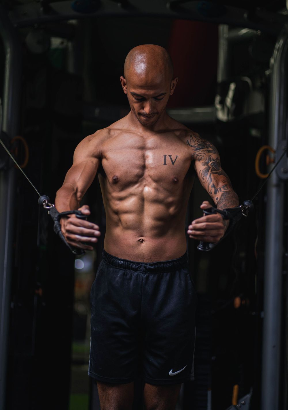 Shirtless athlete using cable machine for upper body workout in gym.