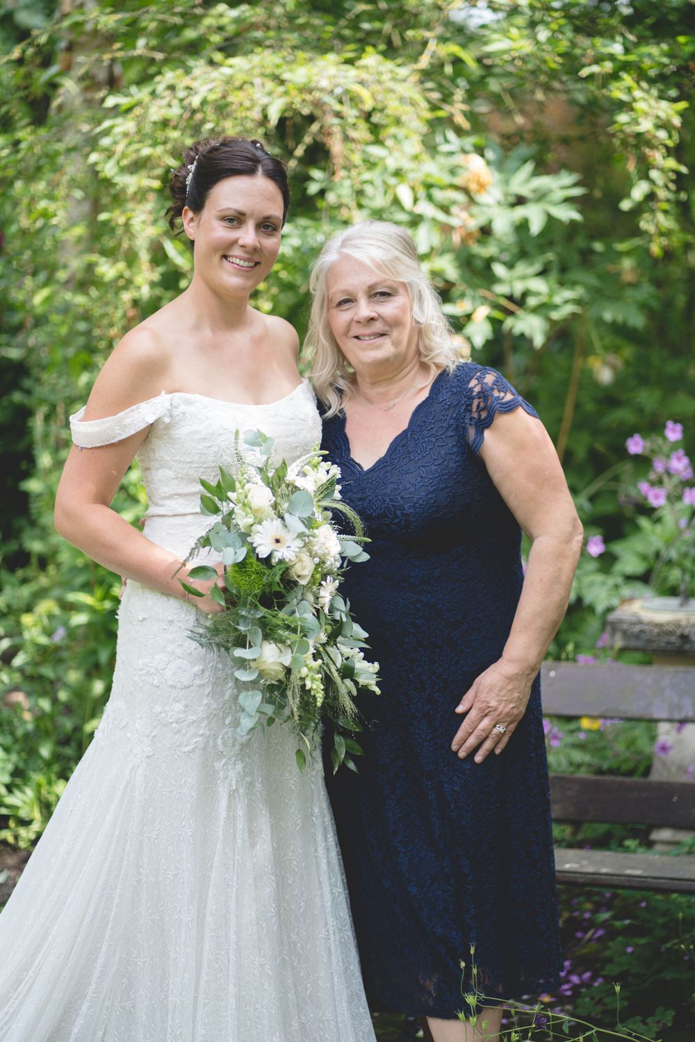 A heartwarming garden wedding photo with two women in formal attire holding a white bouquet.