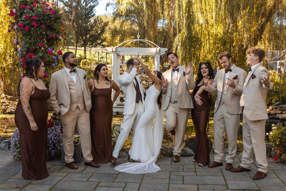 The wedding couple and party celebrate. There are willow trees in the background at The Willows Venue in Central Point, Oregon.