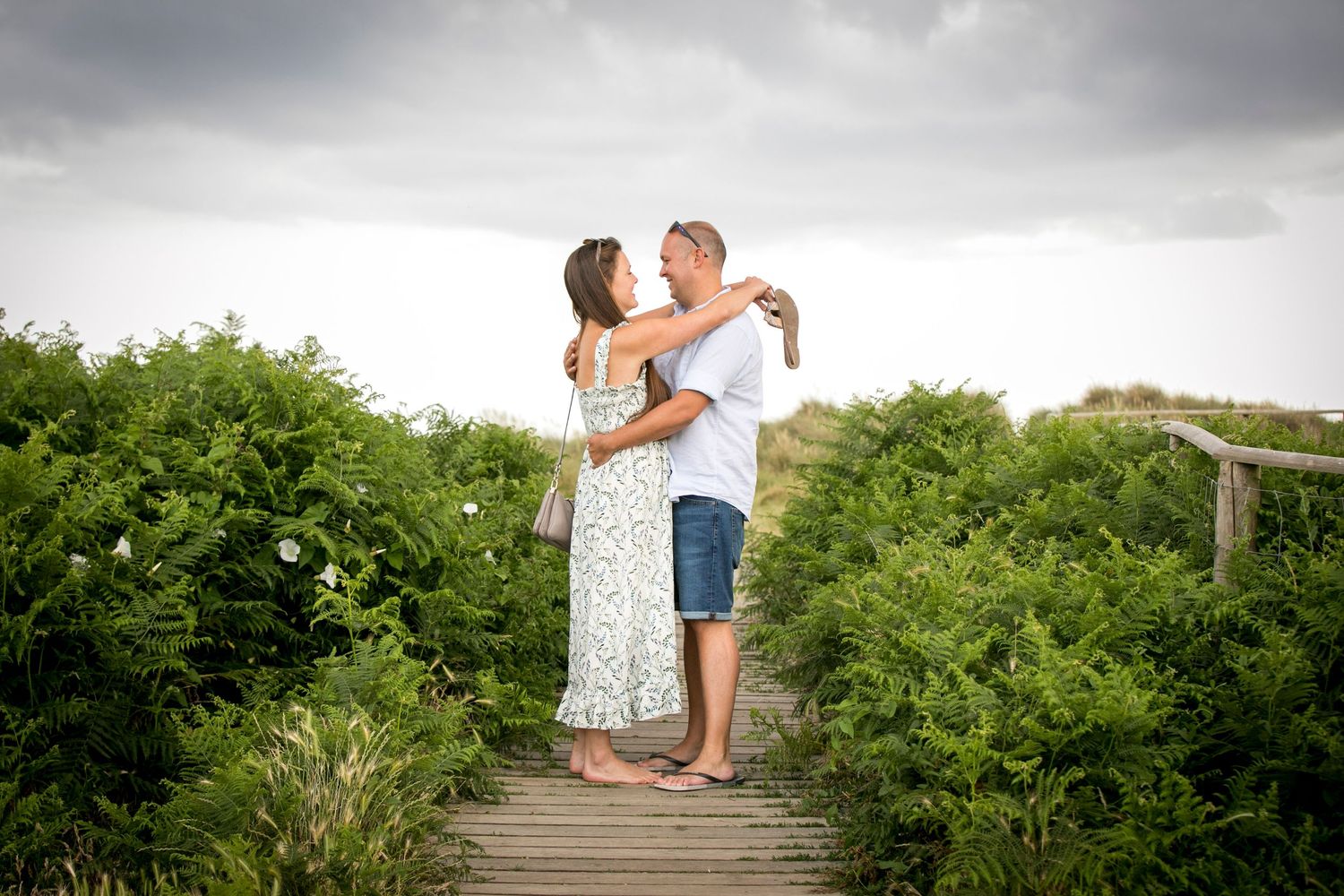Romantic couple posing on grassy coastal dunes with ocean in background.