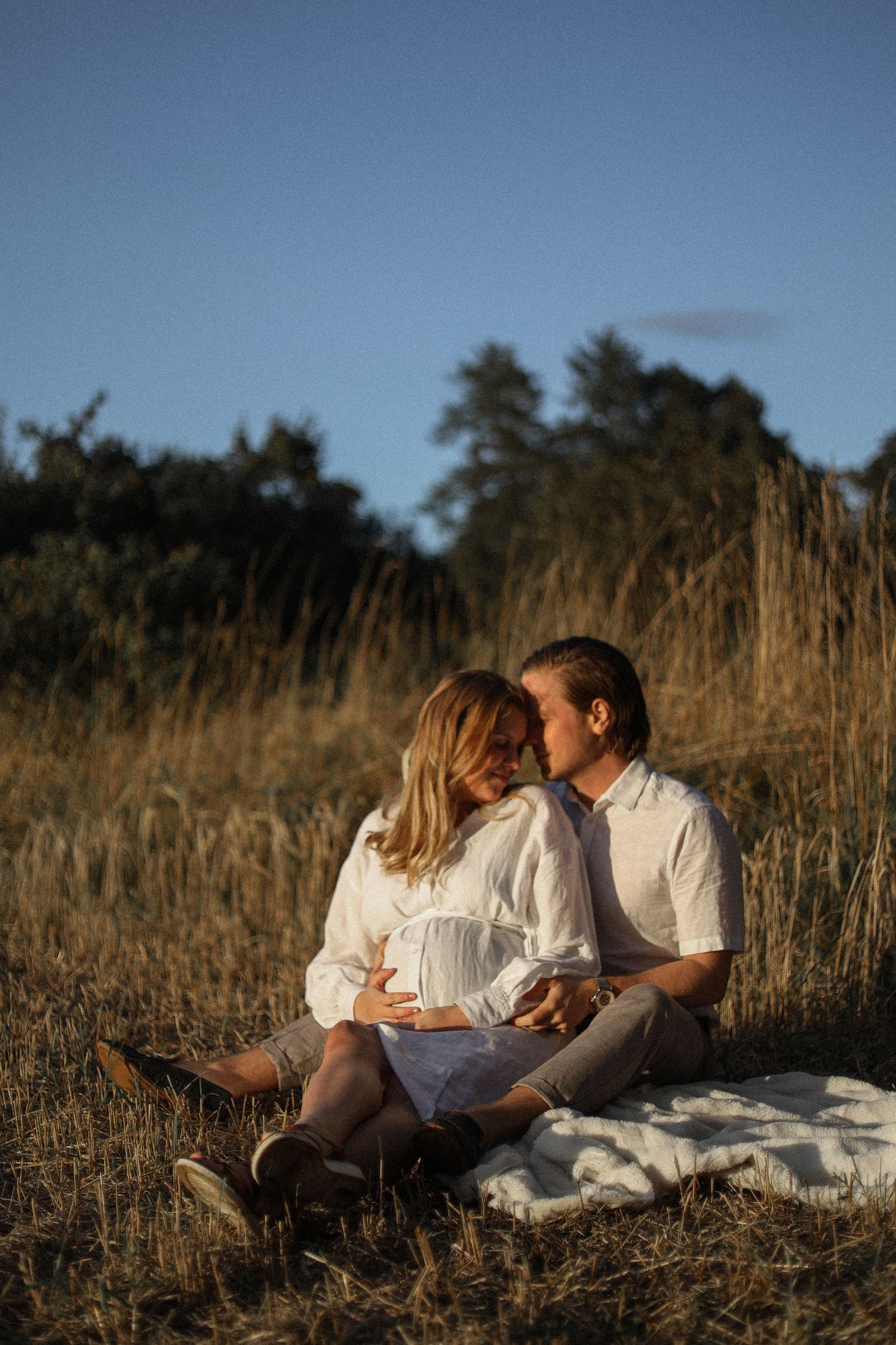 Couple sitting on blanket in tall grass during sunset.