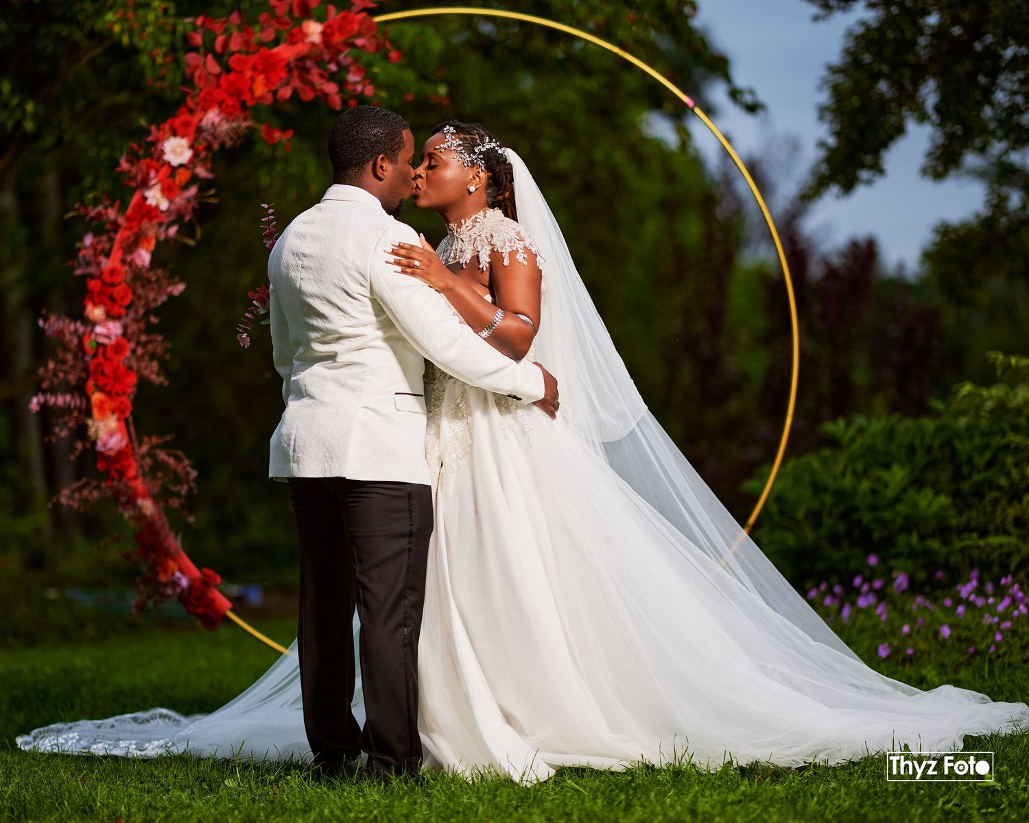 Romantic outdoor wedding portrait of a newlywed couple sharing an intimate moment under a floral arch.