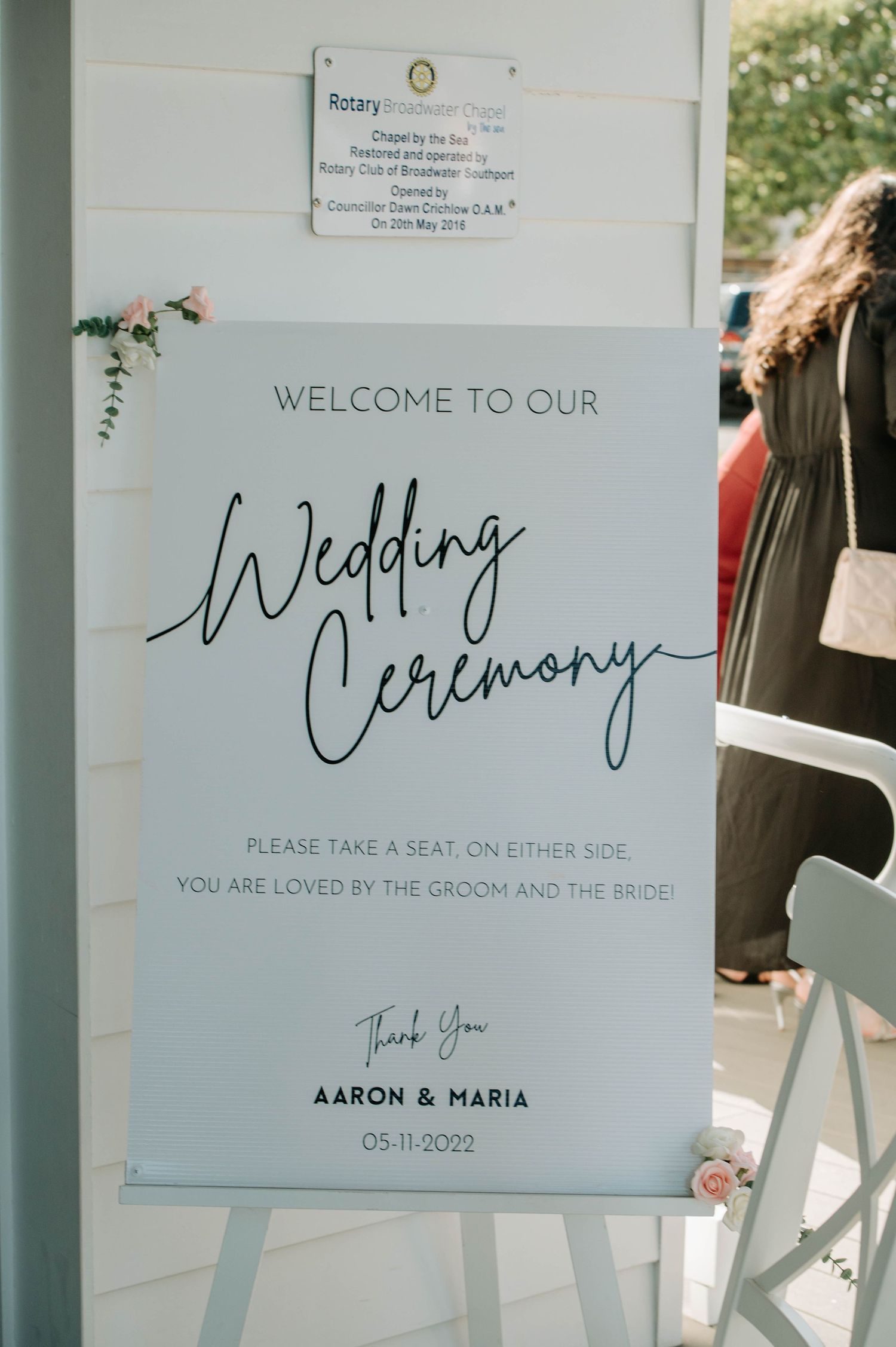 Wedding ceremony welcome sign with elegant script font on white board.