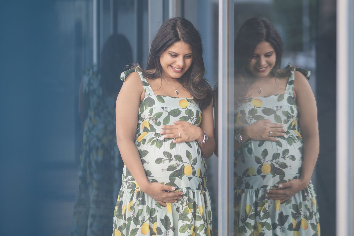 Maternity portrait with reflection showing floral dress and gentle belly touch.
