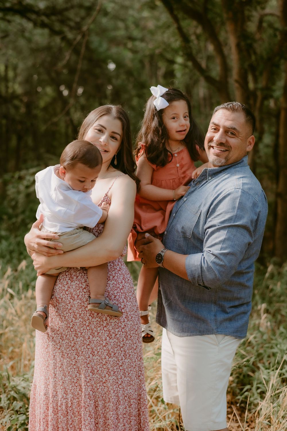 Family of four posing together in wooded area wearing coordinated spring outfits.