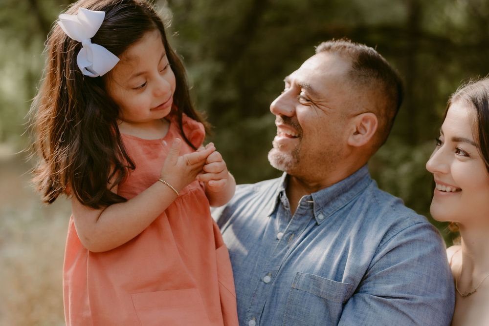 Family sharing tender moment together outdoors with young child in coral dress.