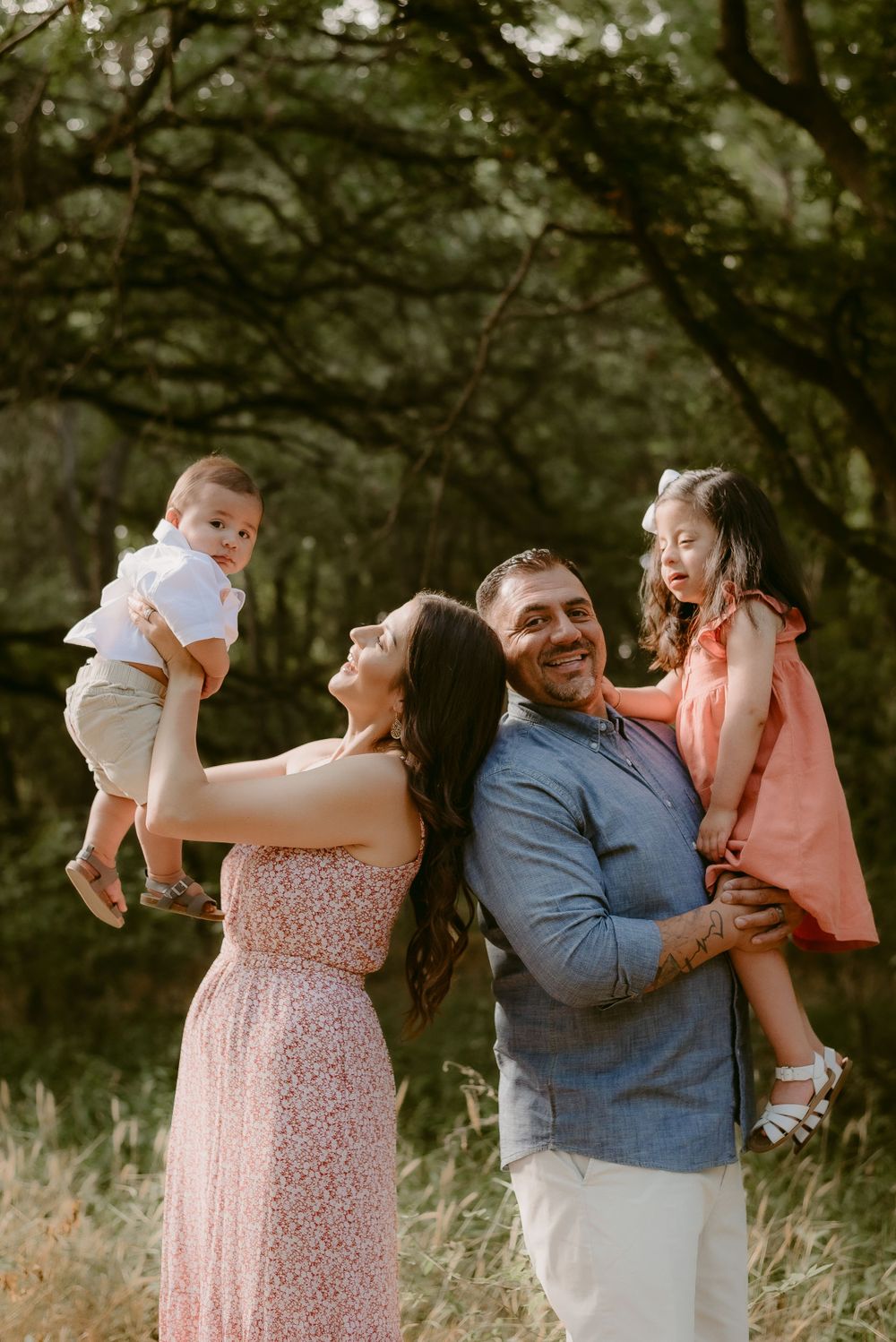 Family playing and laughing together in a wooded setting during golden hour.