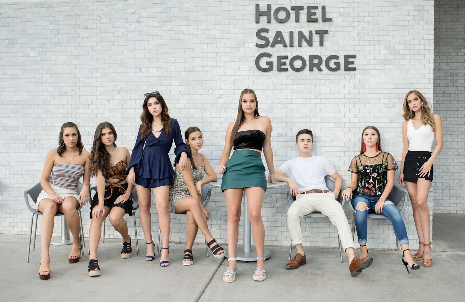 Group posed casually outside the Hotel Saint George building in stylish outfits against a grey stone wall.