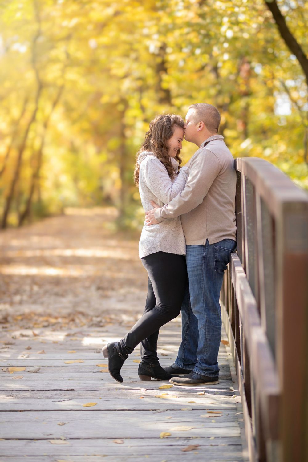 Two people share an intimate moment on a wooden bridge surrounded by autumn foliage.
