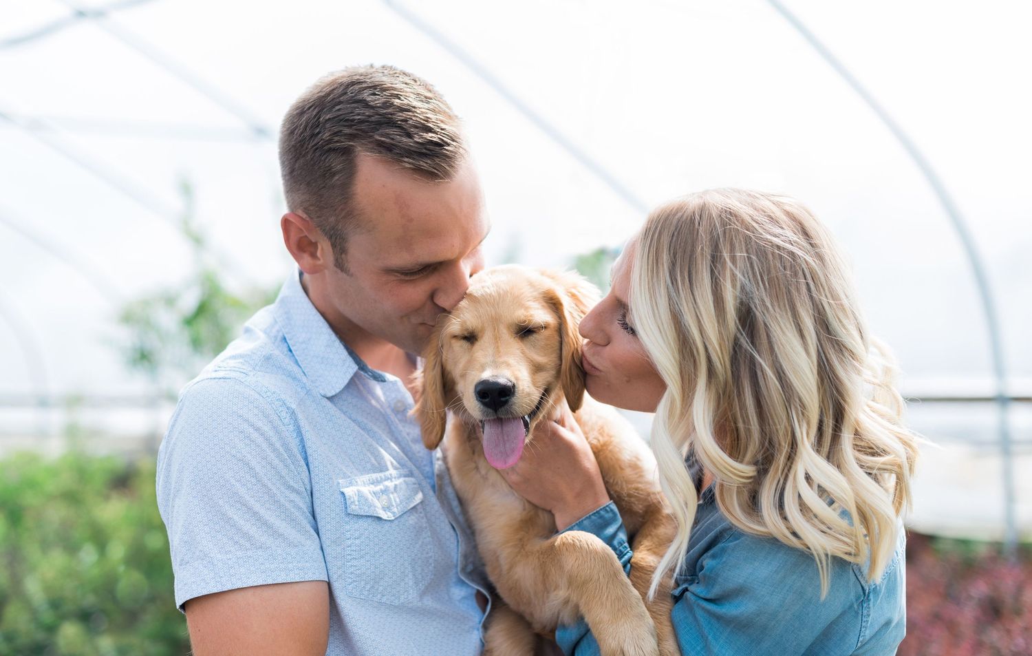 Couple kissing a golden retriever puppy.