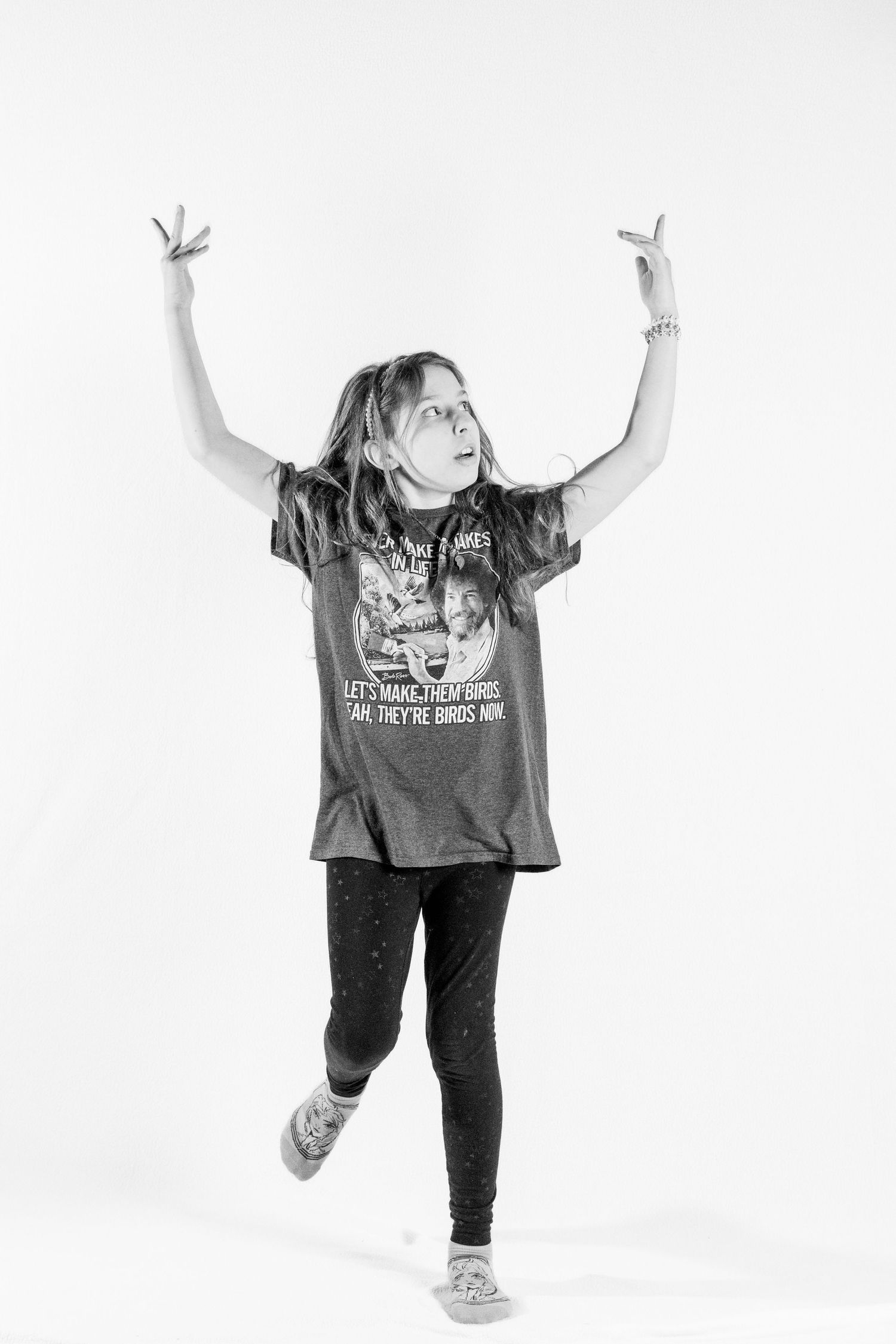 Black and white photo of a young dancer with raised arms wearing a graphic t-shirt.