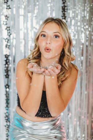 Festive portrait with silver tinsel backdrop and glitter-blowing pose.
