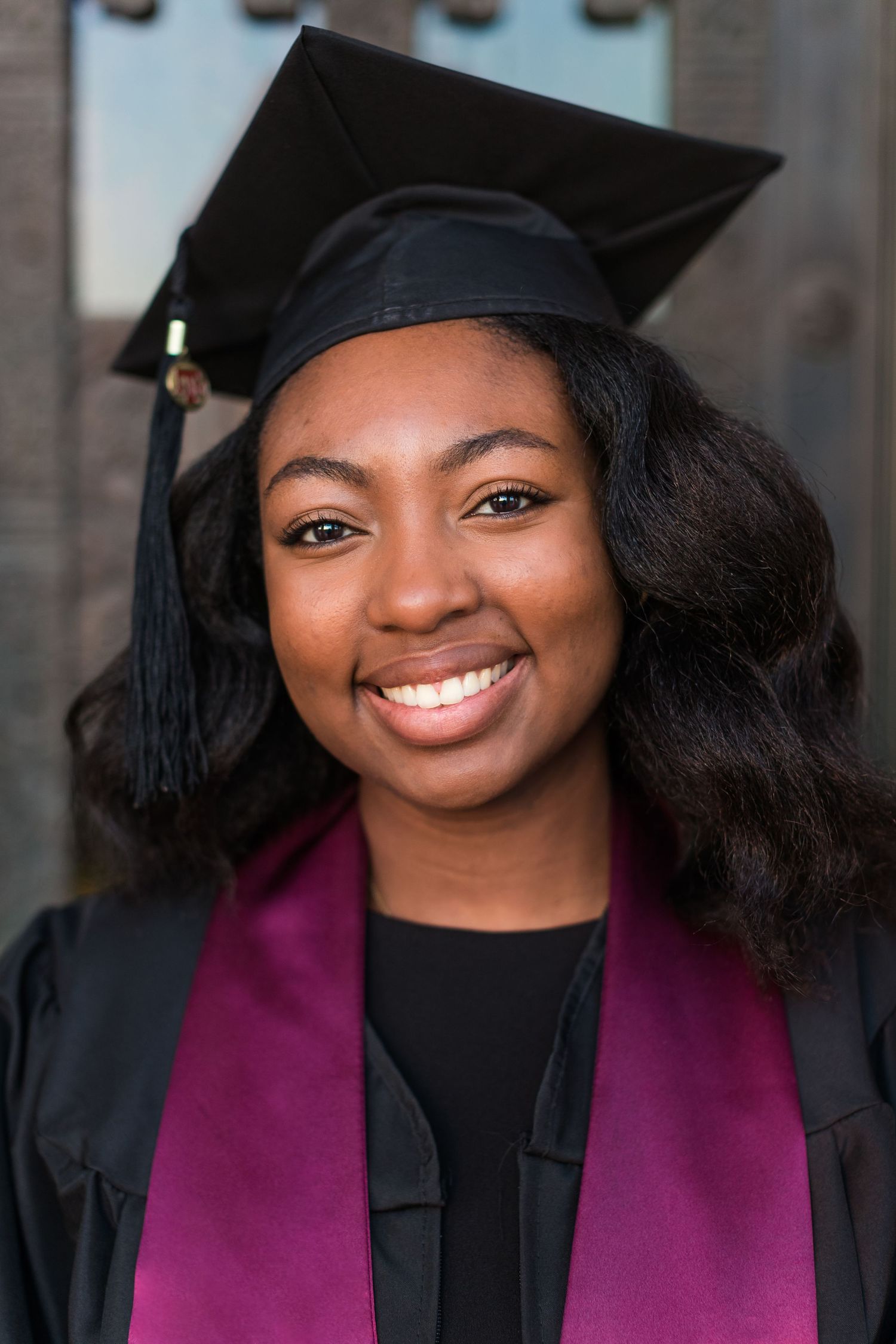 Graduate in cap and gown with burgundy stole smiles during graduation photoshoot.