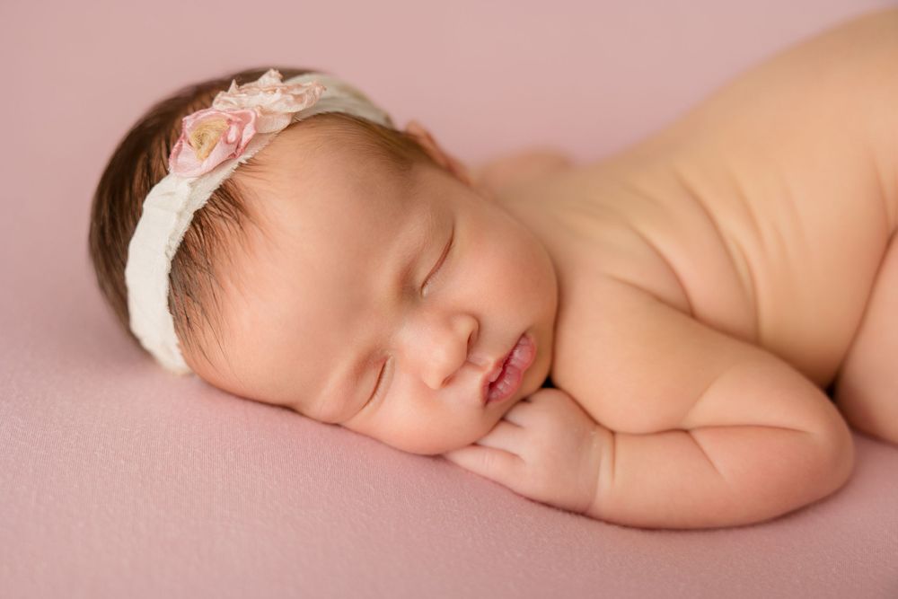 Sleeping newborn with delicate floral headband on pink blanket.