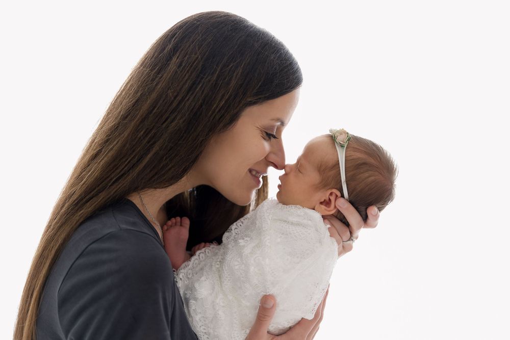 Tender moment between parent and newborn in white dress.