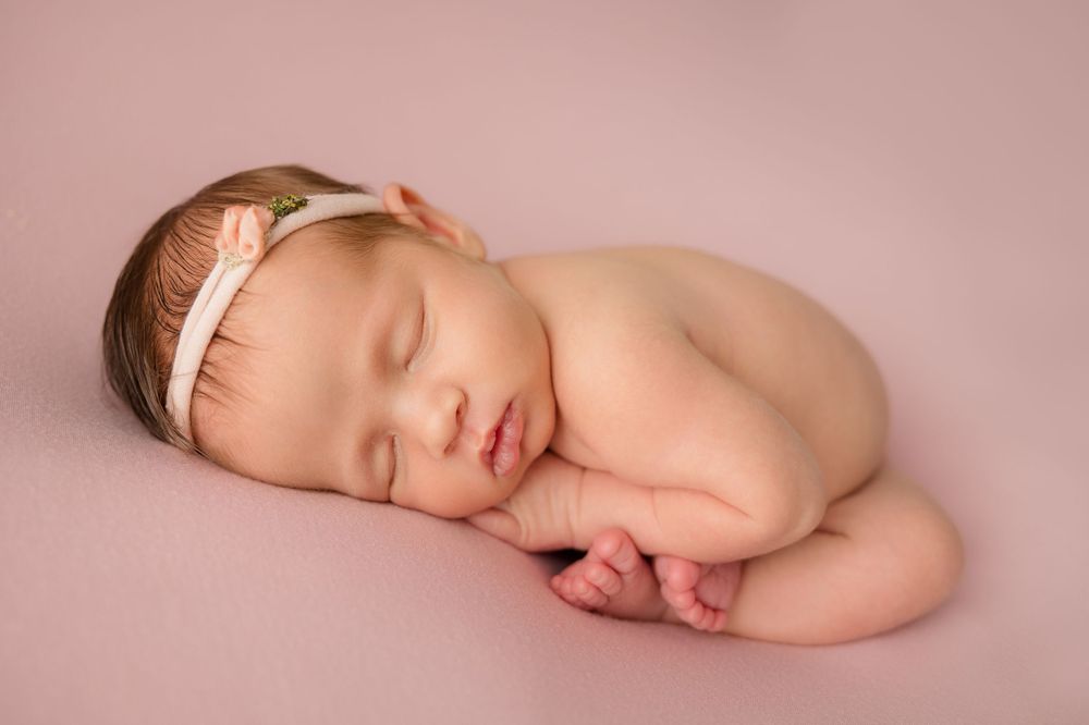Sleeping baby wearing peach headband on pink background.