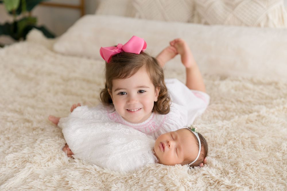 Siblings share sweet moment together on white bedding.