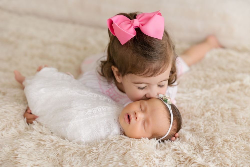 Sweet sibling moment as young child gives baby gentle kiss on white background.