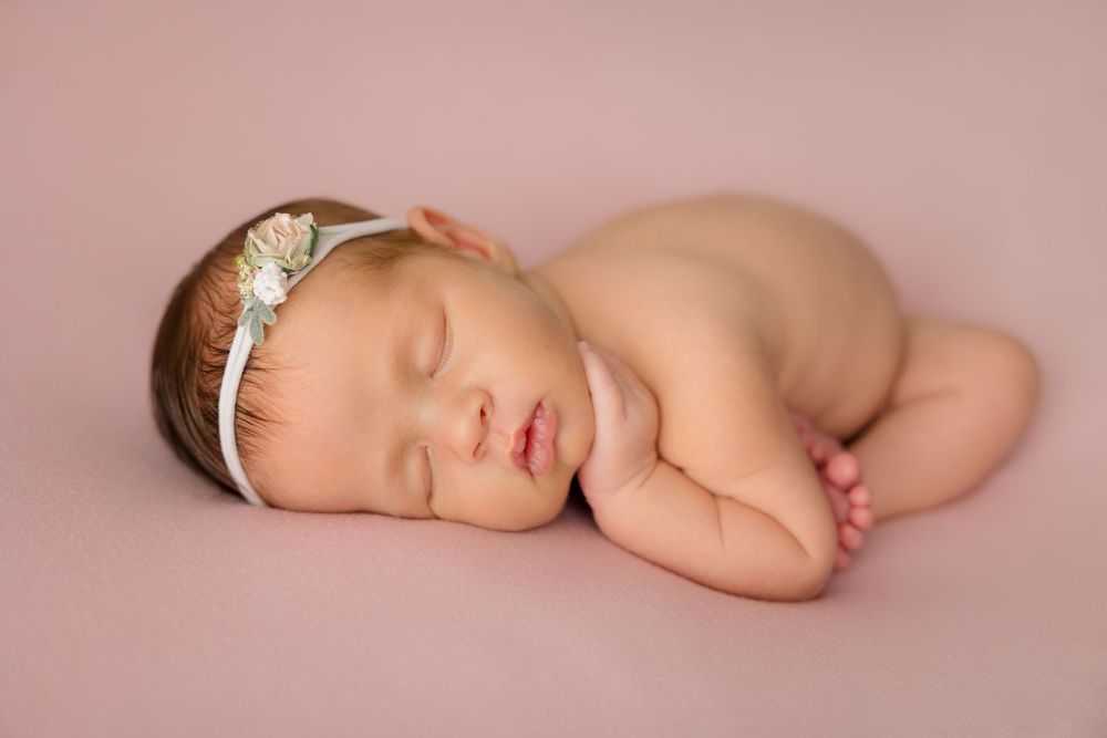 Sleeping newborn with decorative headband posed on pink backdrop.