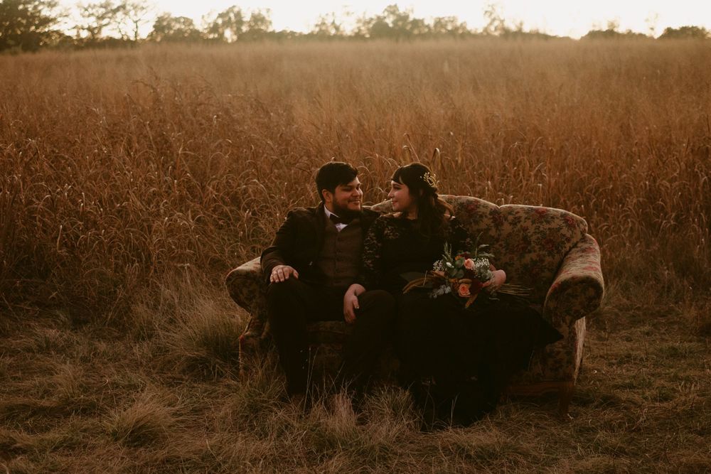 A couple shares an intimate moment on a vintage couch in a golden field at sunset.
