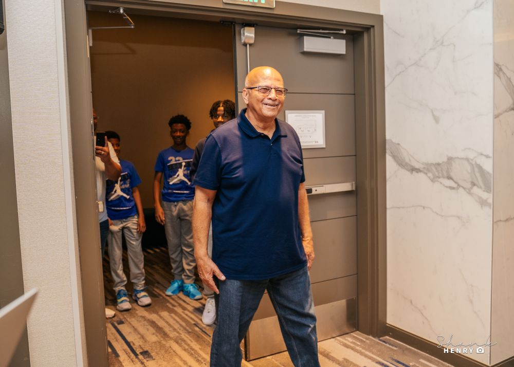 A group gathering in a hallway with marble walls and wooden flooring.