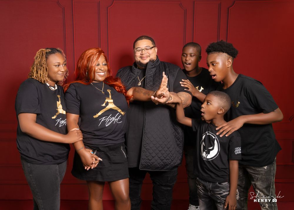 A group wearing matching black t-shirts poses together against a red backdrop.