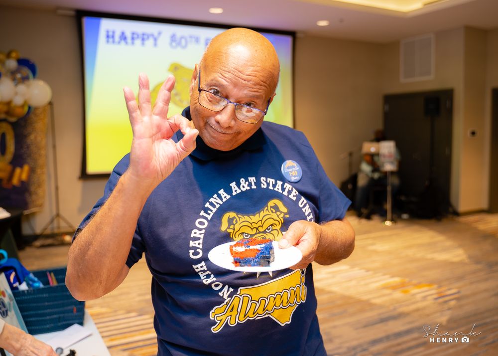 Person wearing navy shirt gestures enthusiastically during presentation with celebration message on screen behind them.