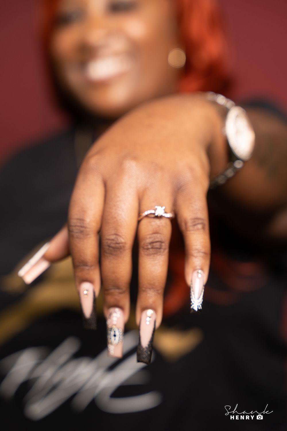 Close-up of an engagement ring and decorated nails against a dark background.