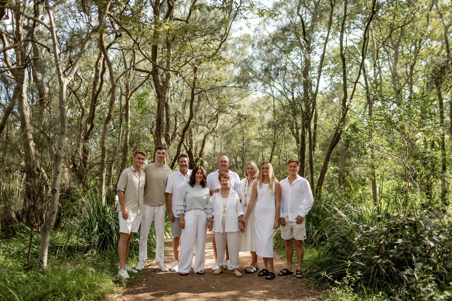 Group photo of people in white clothing on nature trail surrounded by trees.
