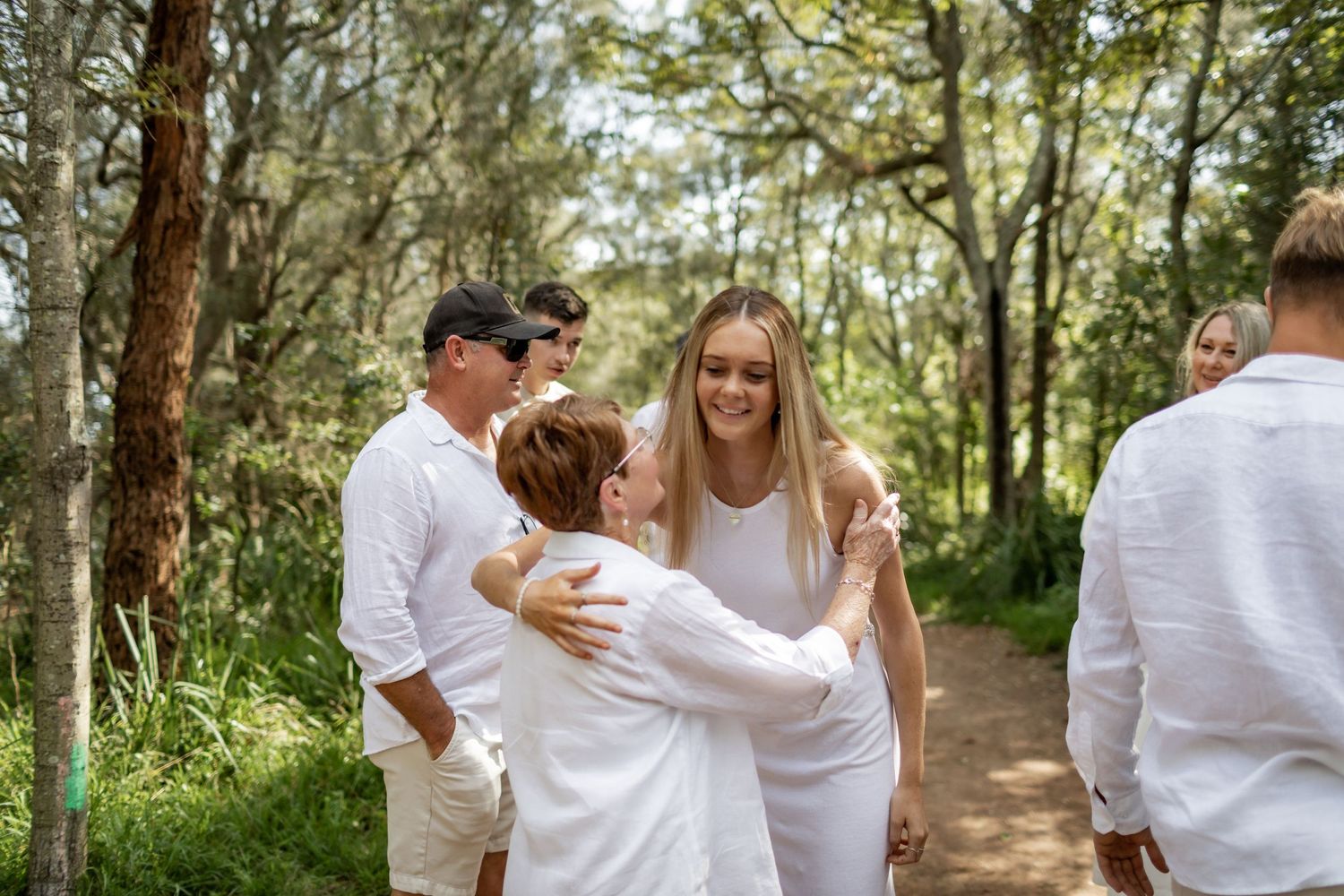 Group walking together on forest trail wearing coordinated white outfits.