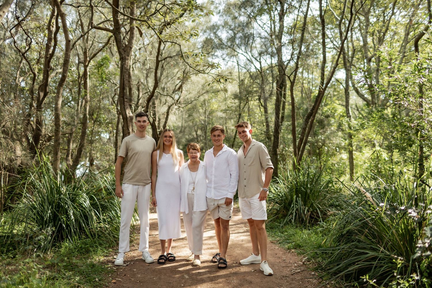 A small group poses together on a nature trail wearing coordinated white and neutral outfits.