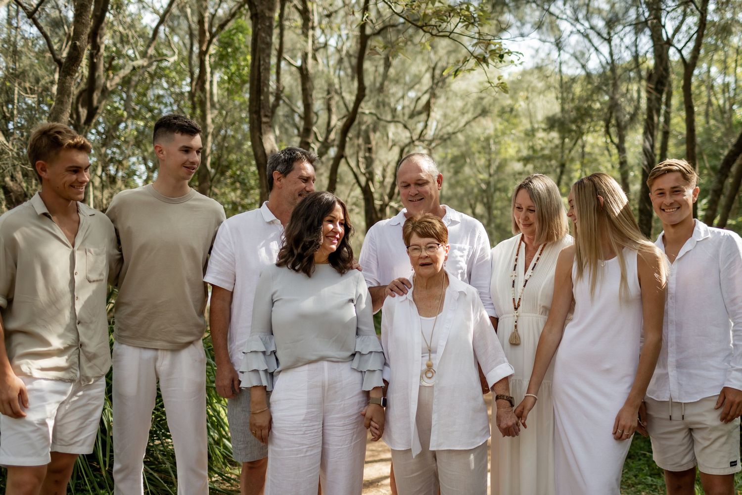 Large group gathered on forest path wearing coordinated white and beige outfits.