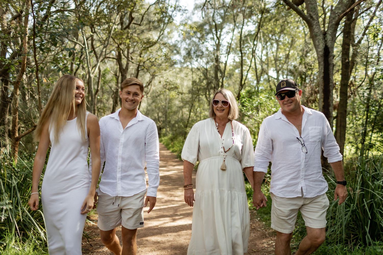 Group walking together on natural path through wooded area wearing white and beige clothing.