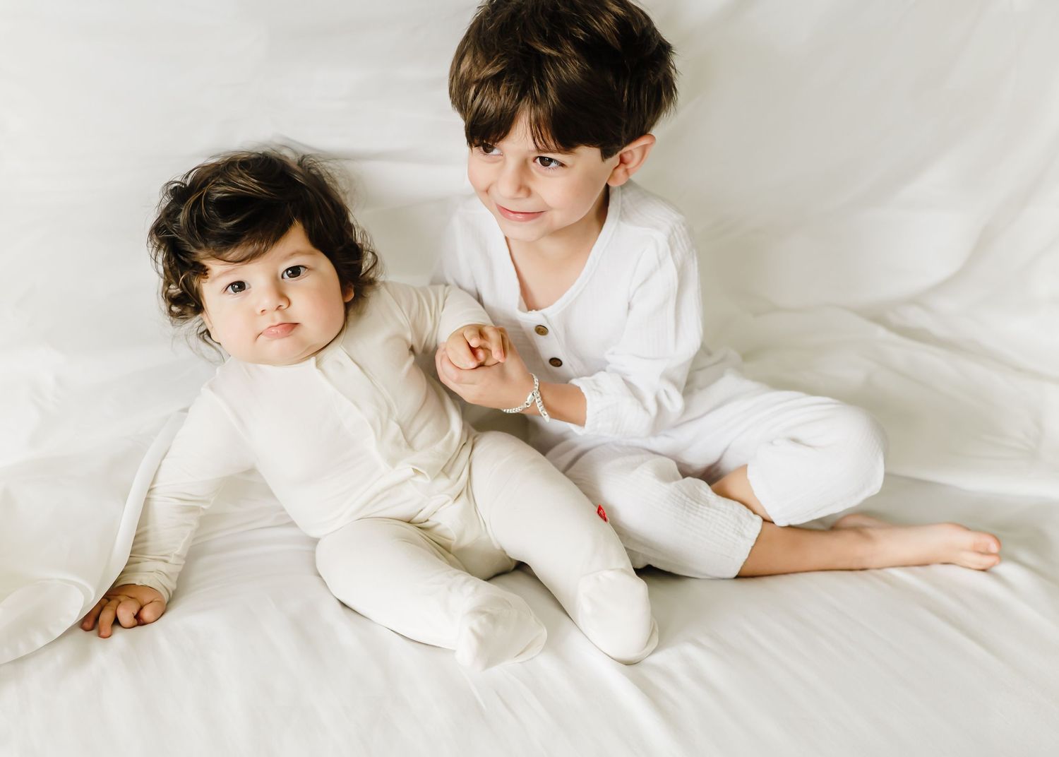 Children in white clothing playing and relaxing on white bedding.