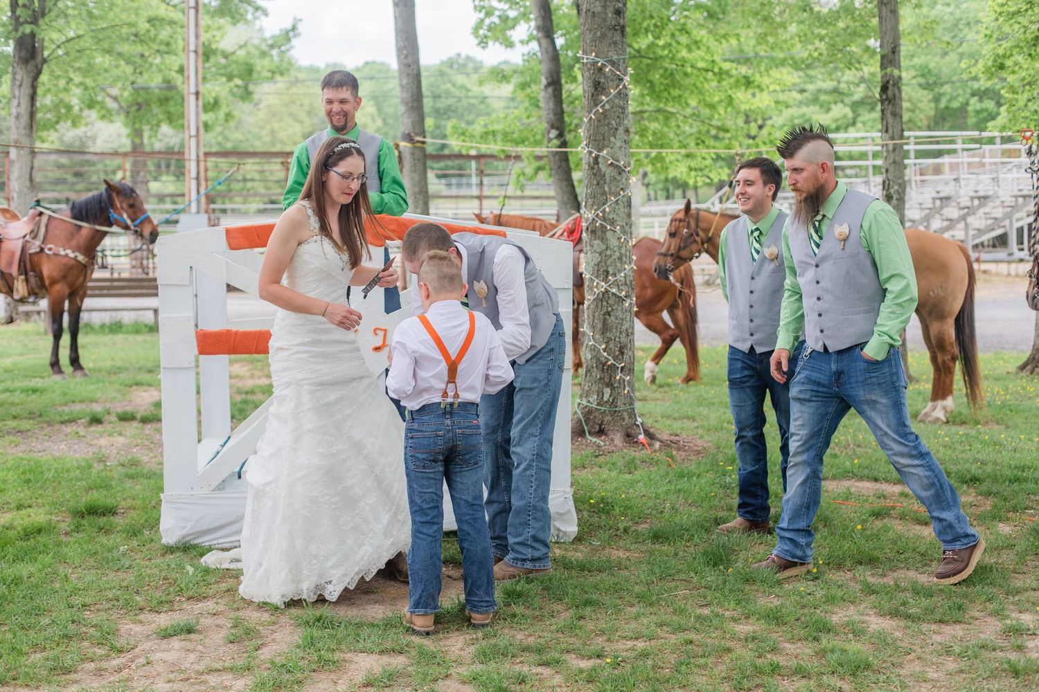 Wedding party members in orange dresses and casual attire gather outdoors under trees.