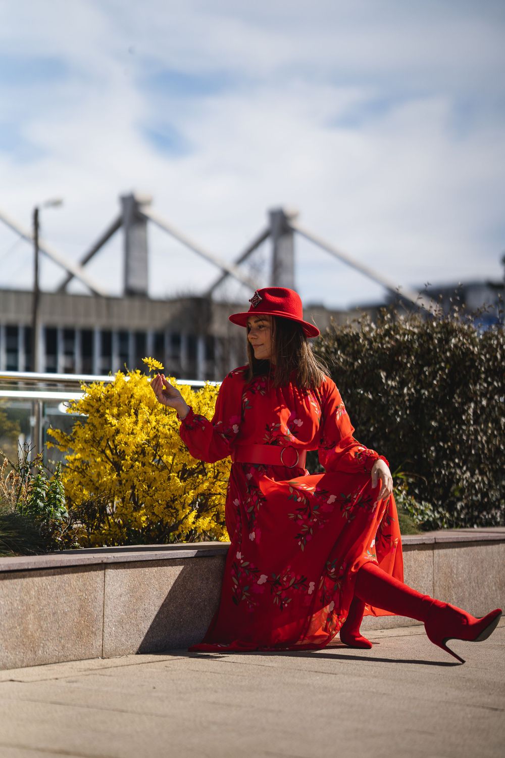 Person in bright red traditional Chinese dress poses near yellow flowers on concrete ledge.
