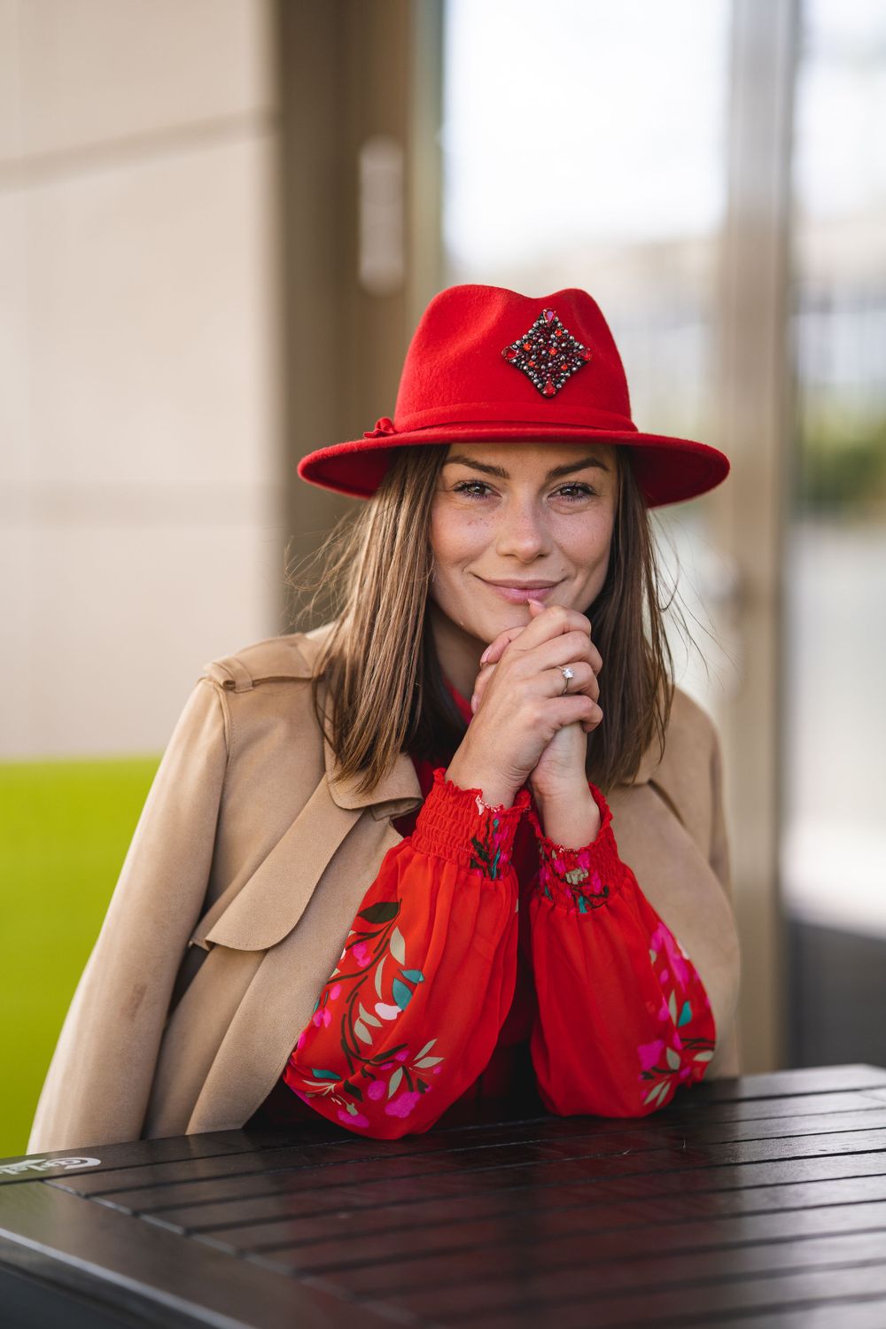 Portrait of person in red hat and beige coat leaning on dark table.