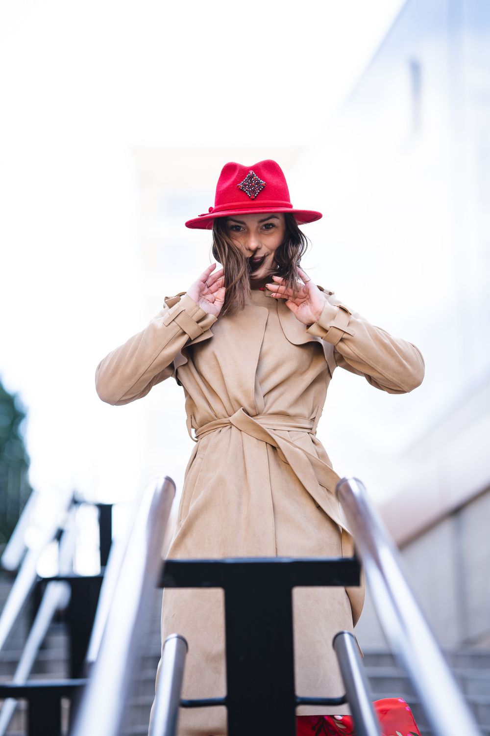 Fashion model in beige coat and red hat posing dramatically outdoors.