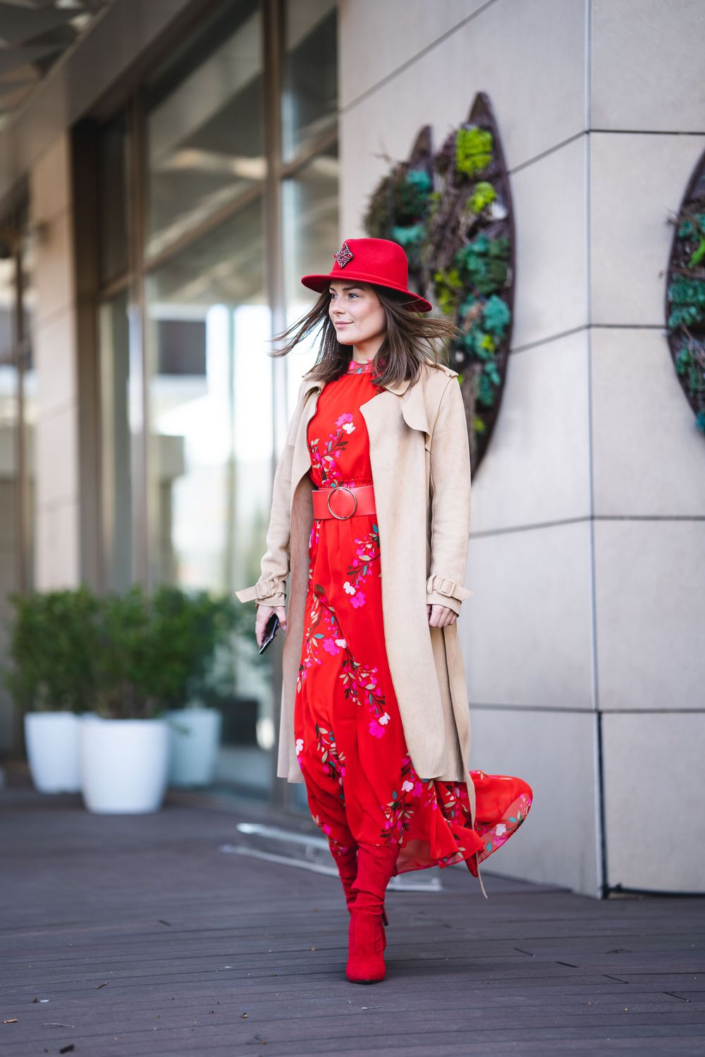 Fashion model in red floral dress, beige trench coat and matching red hat and boots.