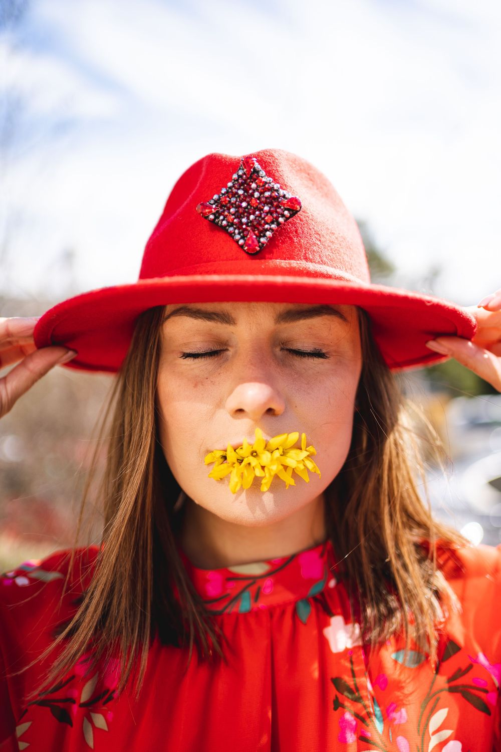 Creative portrait with yellow flower petals placed on lips against red outfit and hat.