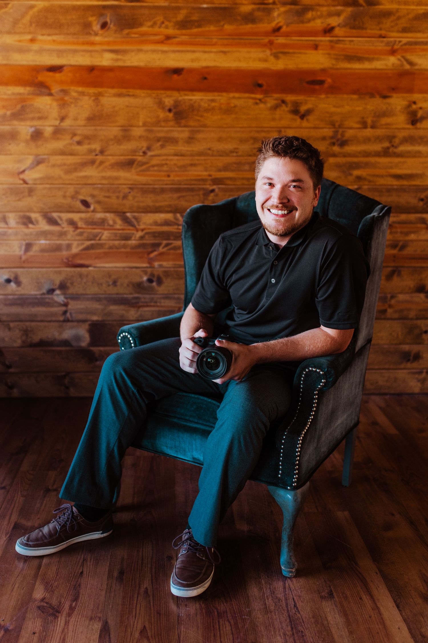 The photographer of Nine13 Studios sitting in a black arm chair holding his camera.