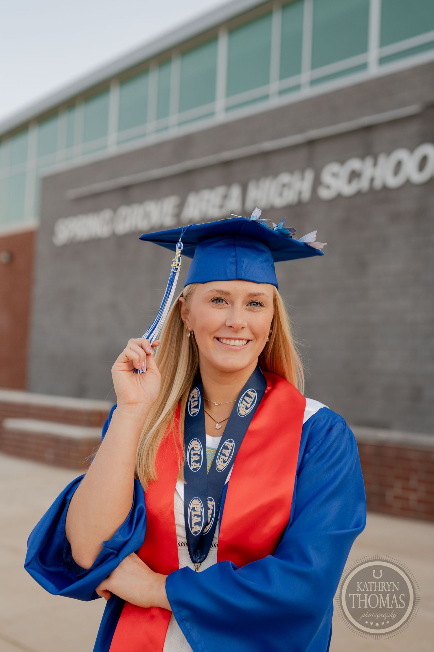 Graduate in blue cap and gown poses with tassel outside Spring Grove Area High School.