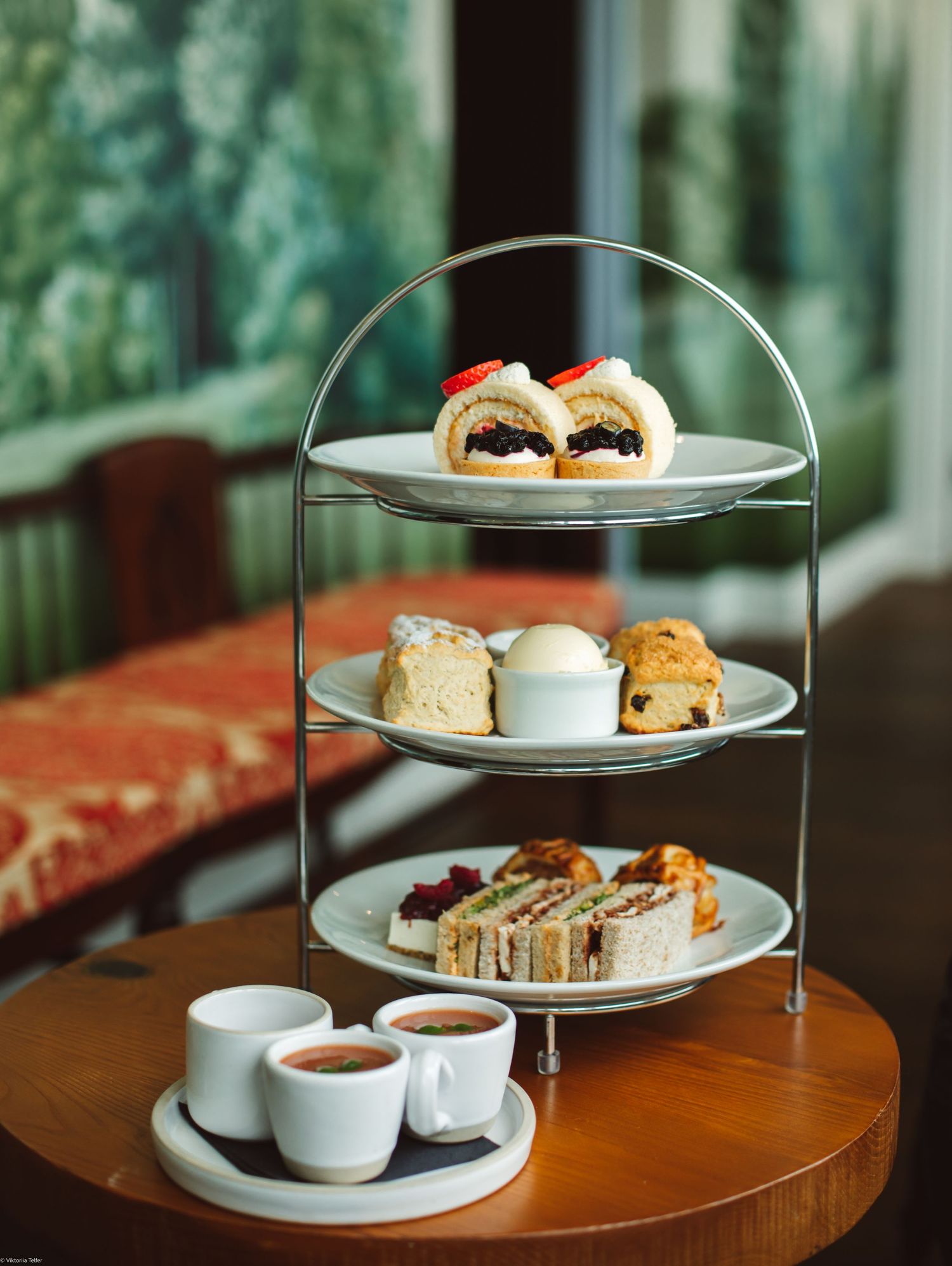 Elegant afternoon tea service with tiered stand displaying scones and sandwiches on wooden table.