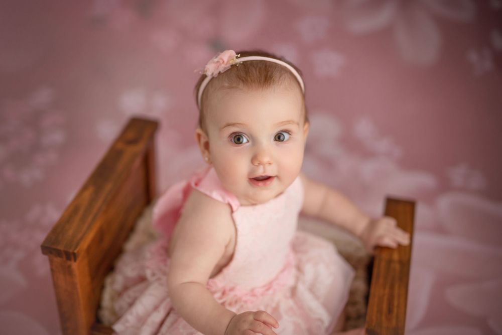 Baby in pink tulle dress sitting in wooden chair.