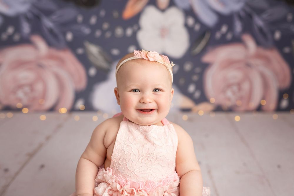 Baby in pink dress against floral wallpaper backdrop.
