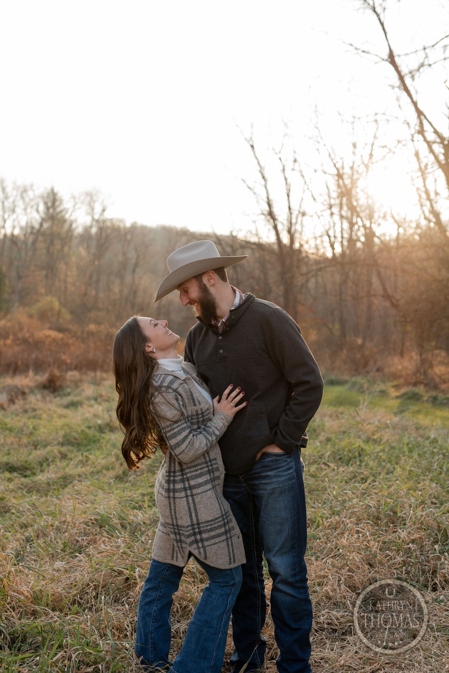 A couple shares an intimate moment outdoors at golden hour with bare trees in the background.
