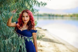 Portrait of person in blue formal dress posing near willow tree by lakeside.